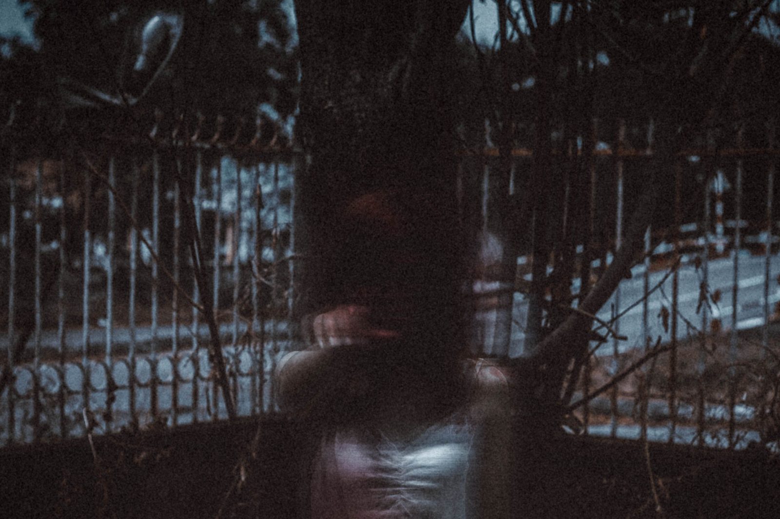 A blurred ghostly figure behind a wrought-iron fence at dusk