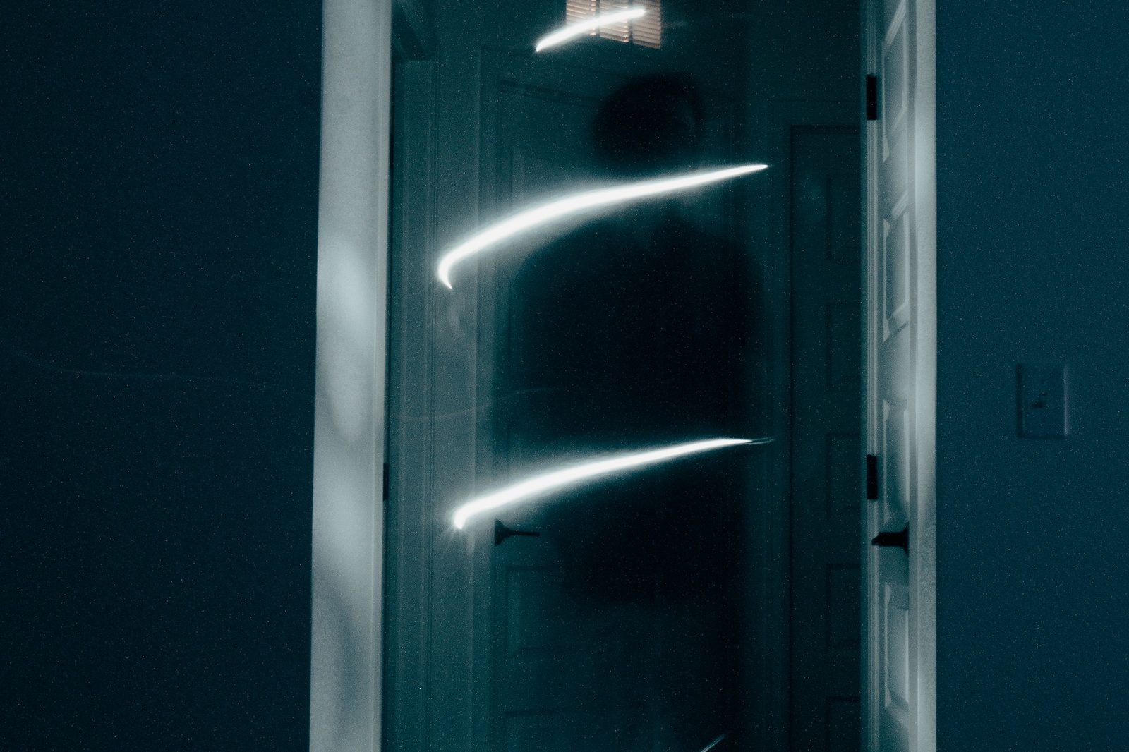 Glowing light trails and a shadowy figure in a darkened hallway