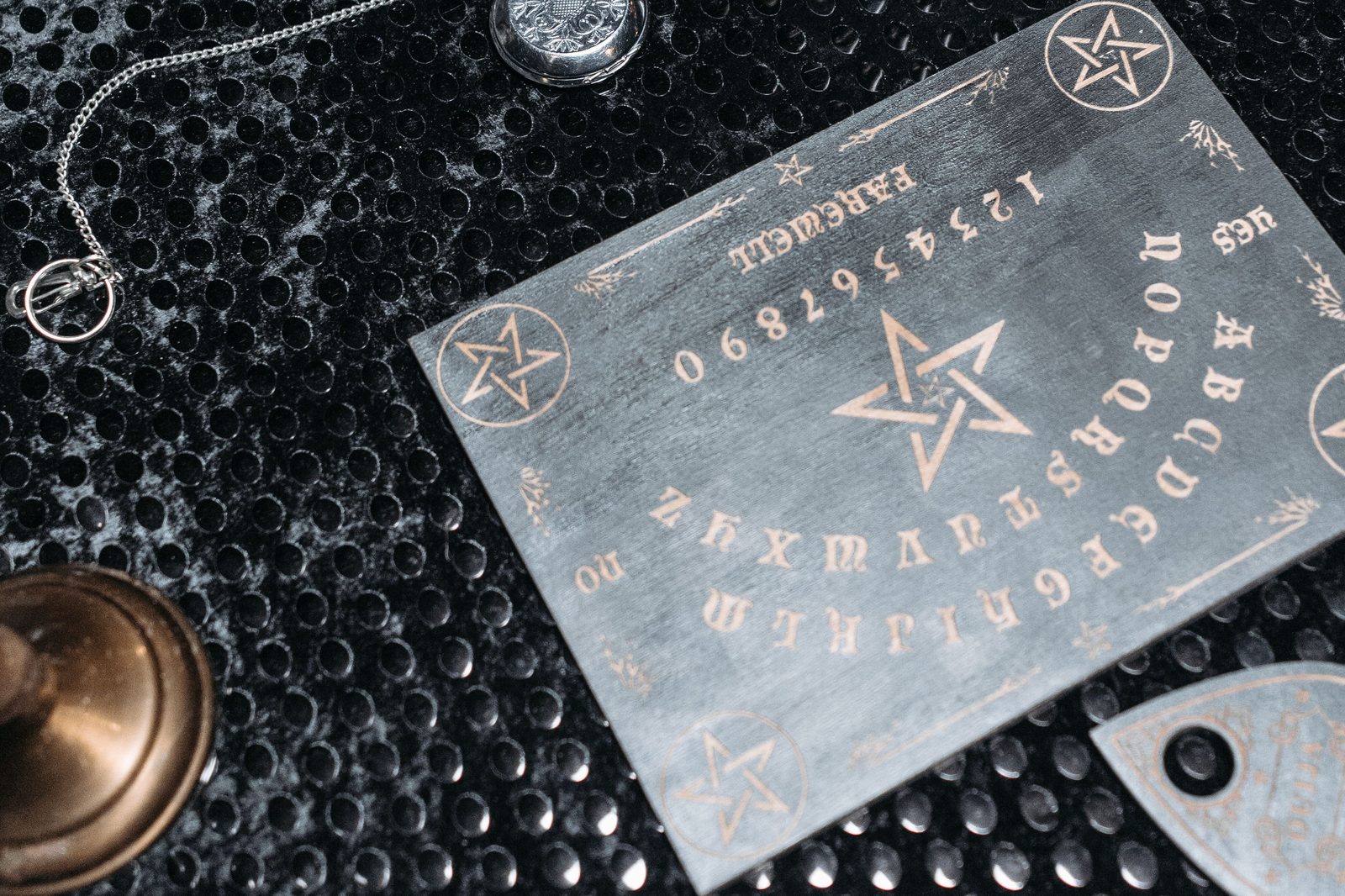 A Ouija board flat-lay with a brass bell, pocket watch, and pendant necklace